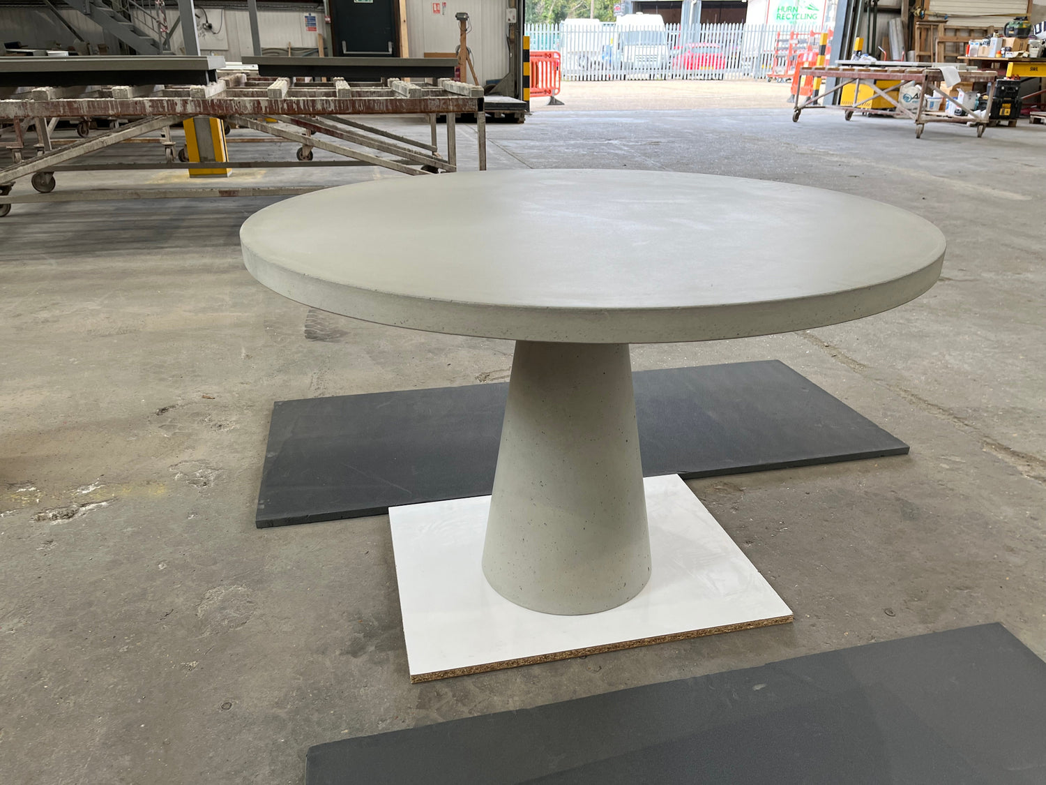 Concrete dining table with pedestal base on a concrete floor in an industrial setting