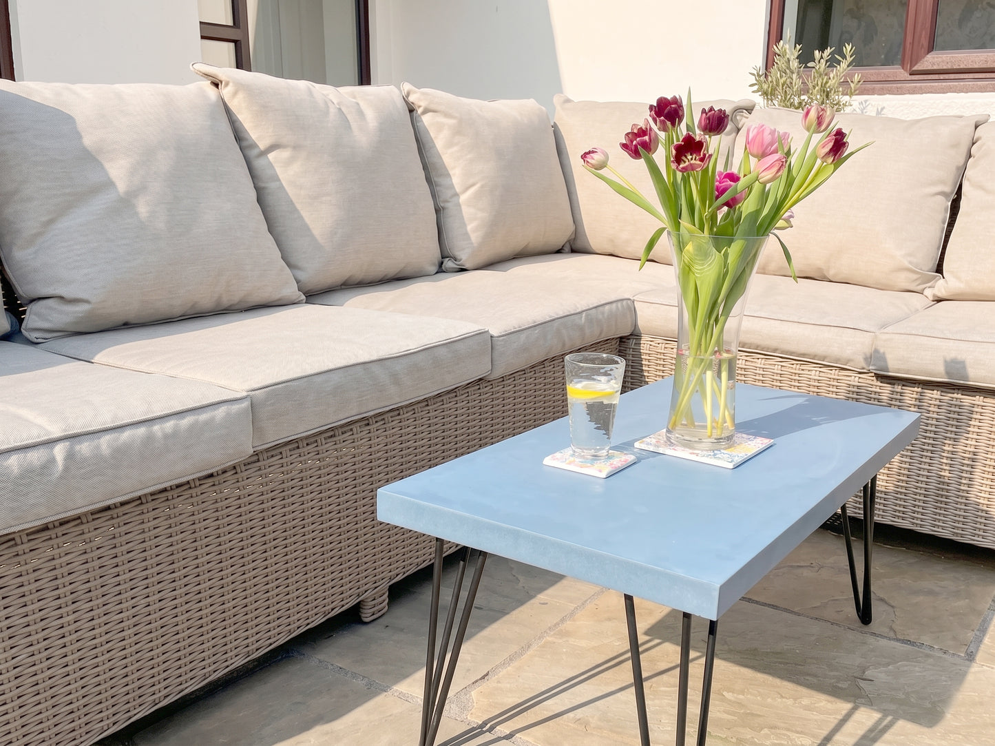 Outdoor patio set with a blue table, beige sofa, and a vase of flowers.