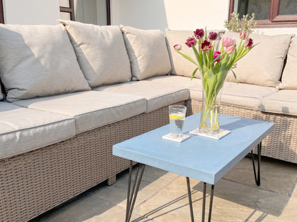Outdoor patio set with a blue table, beige sofa, and a vase of flowers.