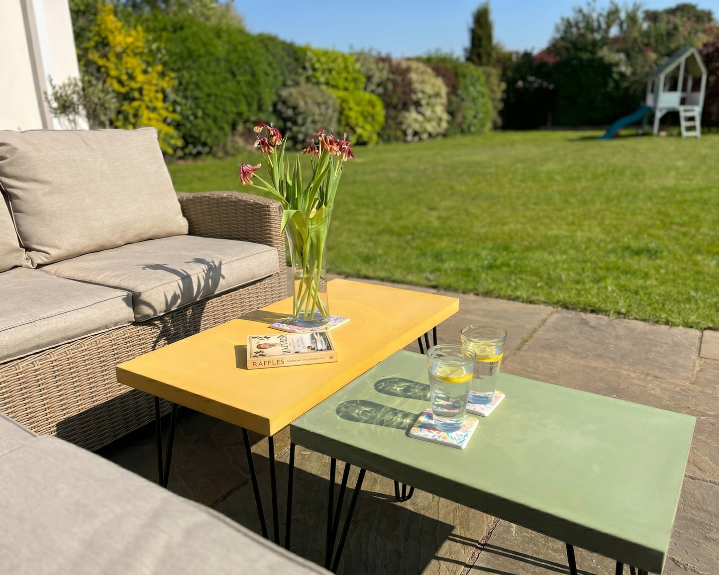 Outdoor patio setting with wicker furniture, yellow table, green table, and flowers.