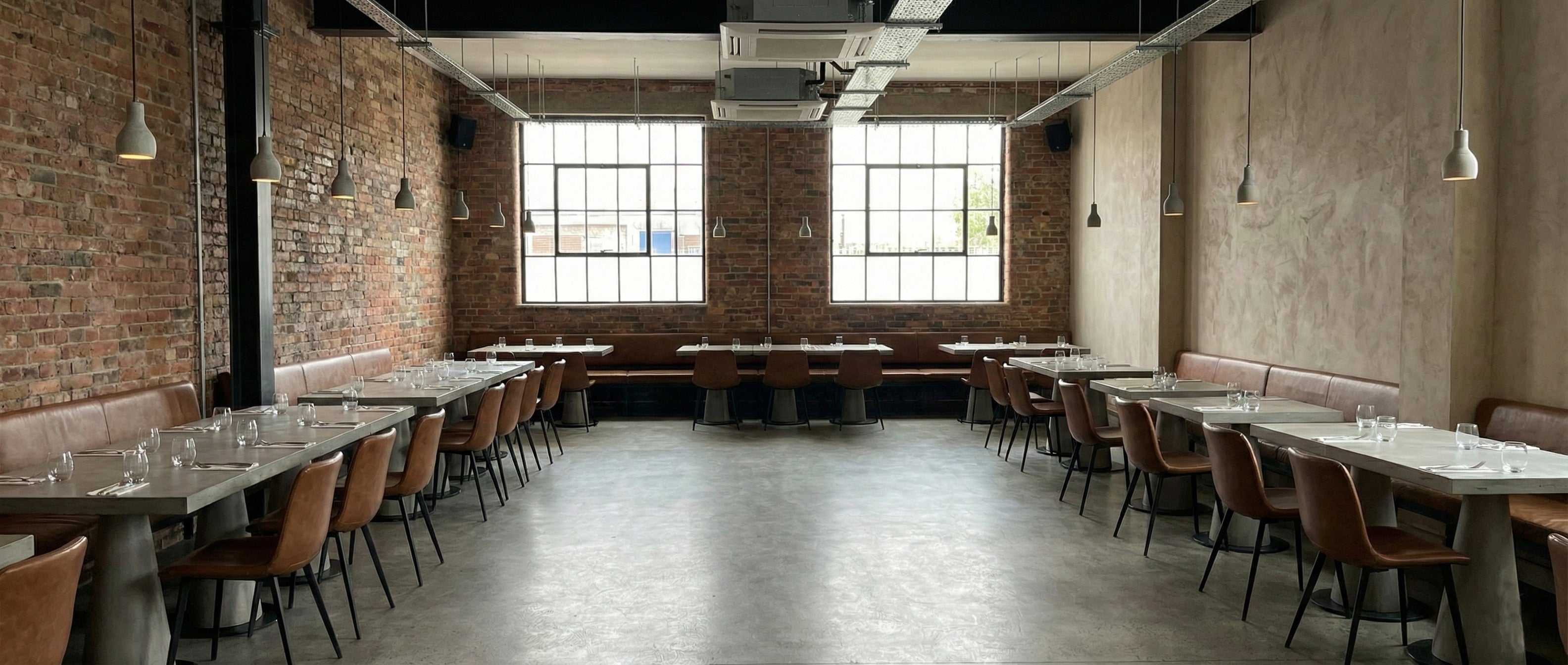 Large dining area with brick walls, large windows, and concrete tables and chairs.