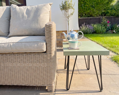 Outdoor patio setting with wicker sofa and concrete side table with teapot and cup.