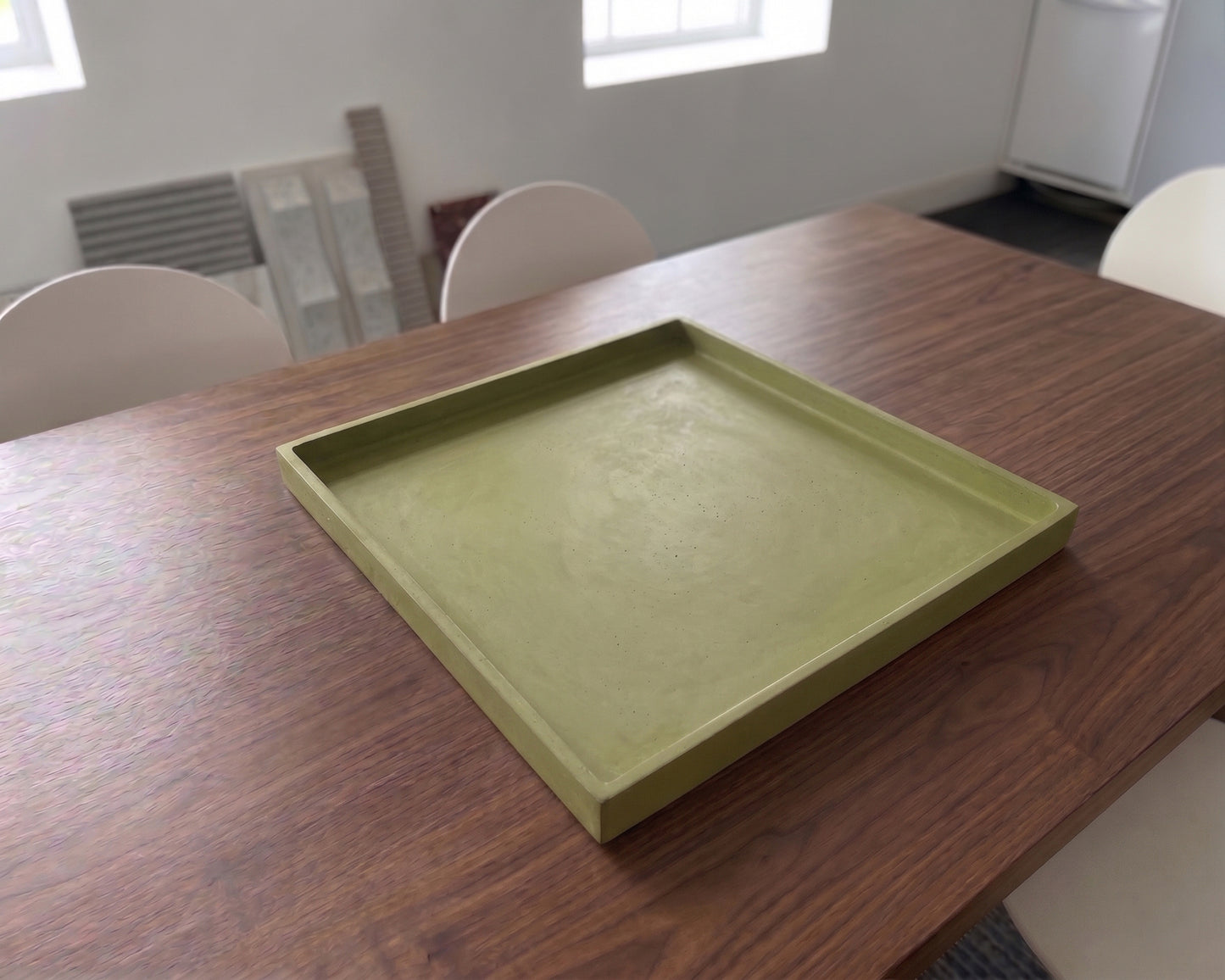 Green tray on a wooden table in a room with chairs and a window.