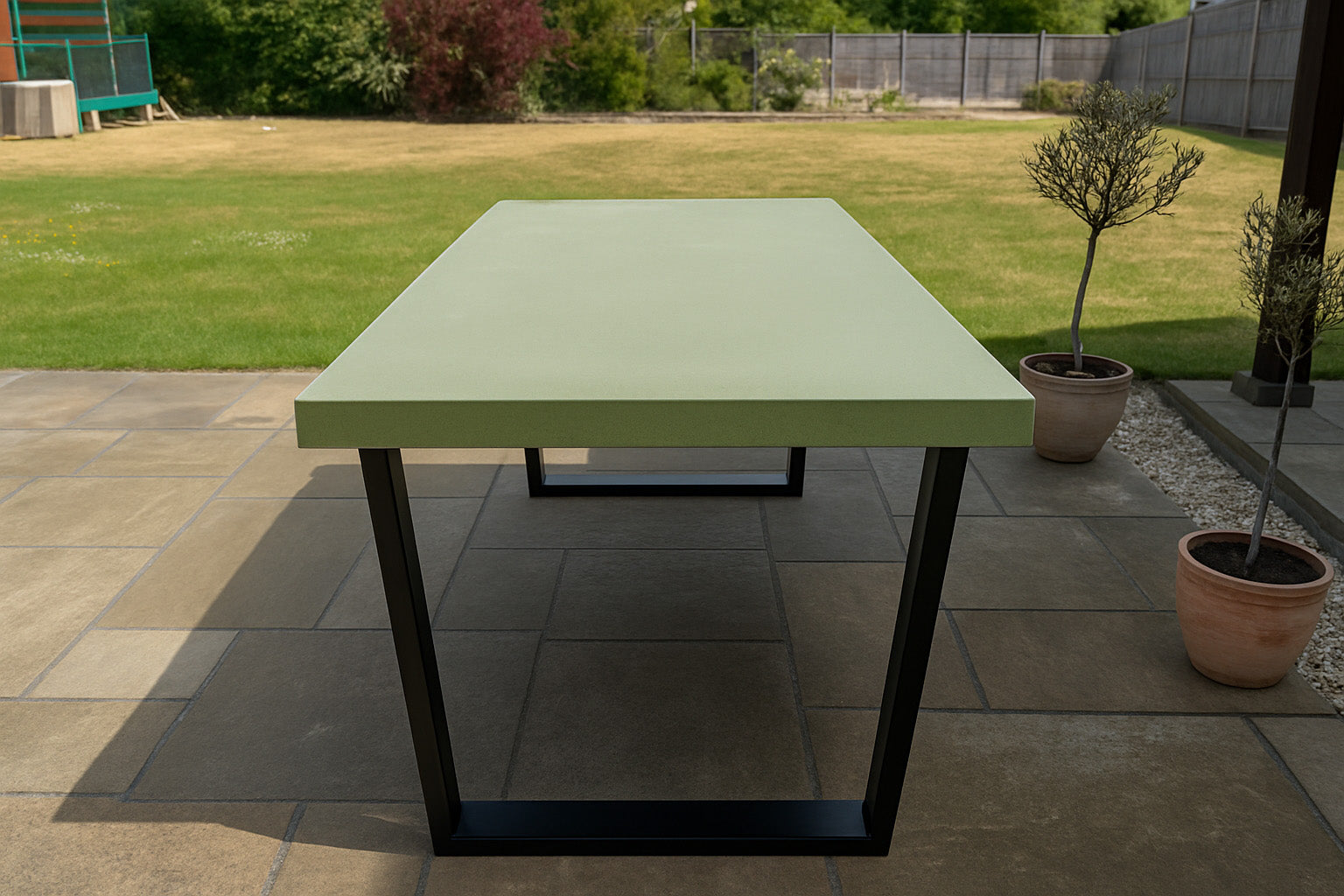 Green outdoor table on a patio with grass and plants in the background