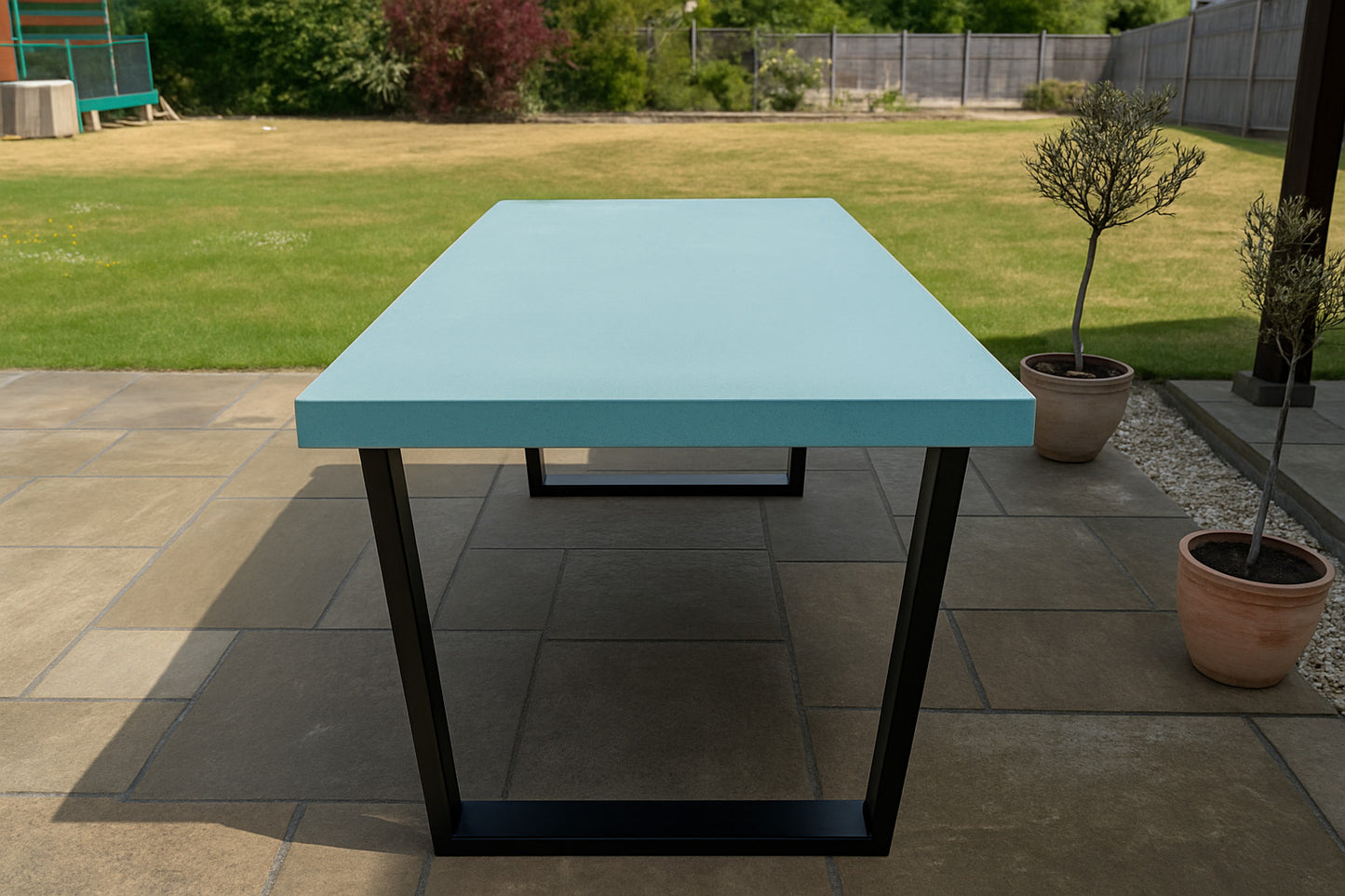 Turquoise table with black legs on a patio area with potted plants and grass in the background