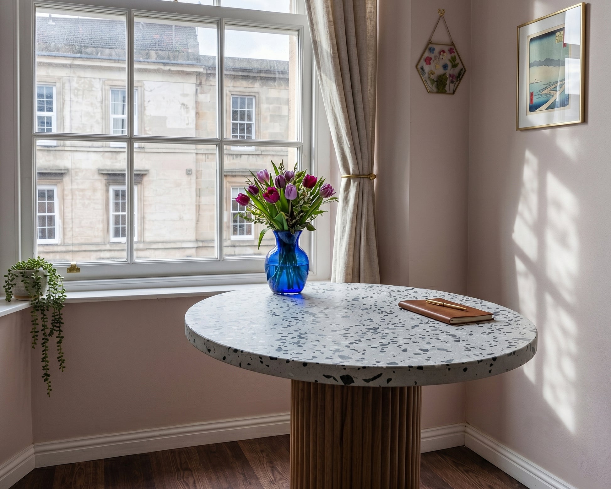 Round concrete grc terrazzo table with a vase of flowers in a room with large windows.