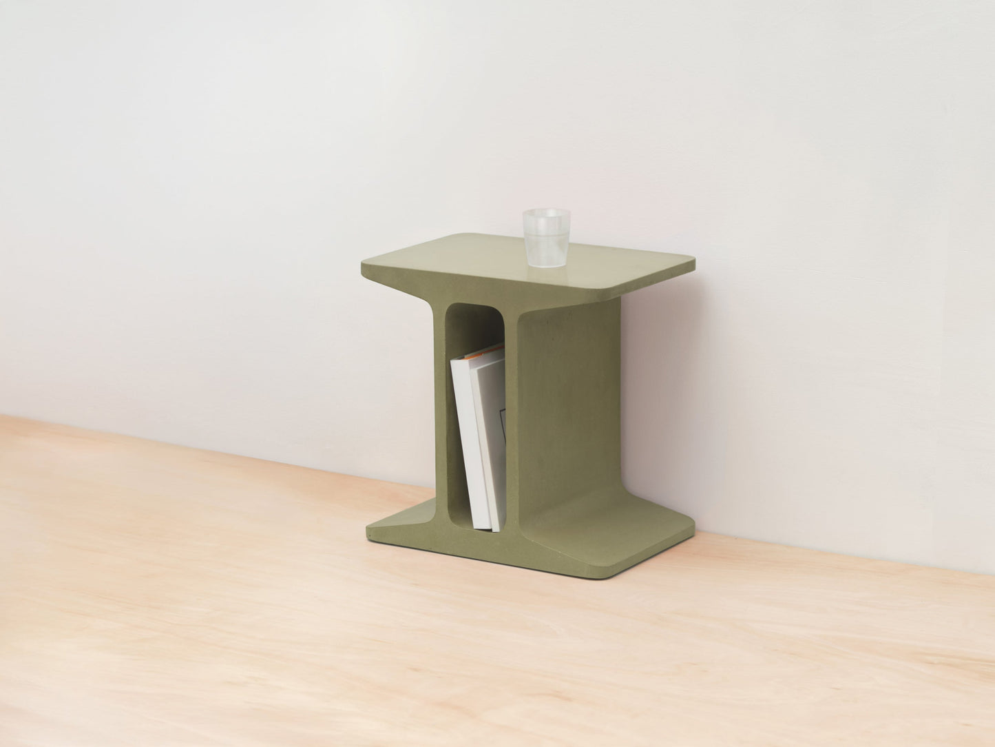 Green side table with a book on a wooden floor against a white wall