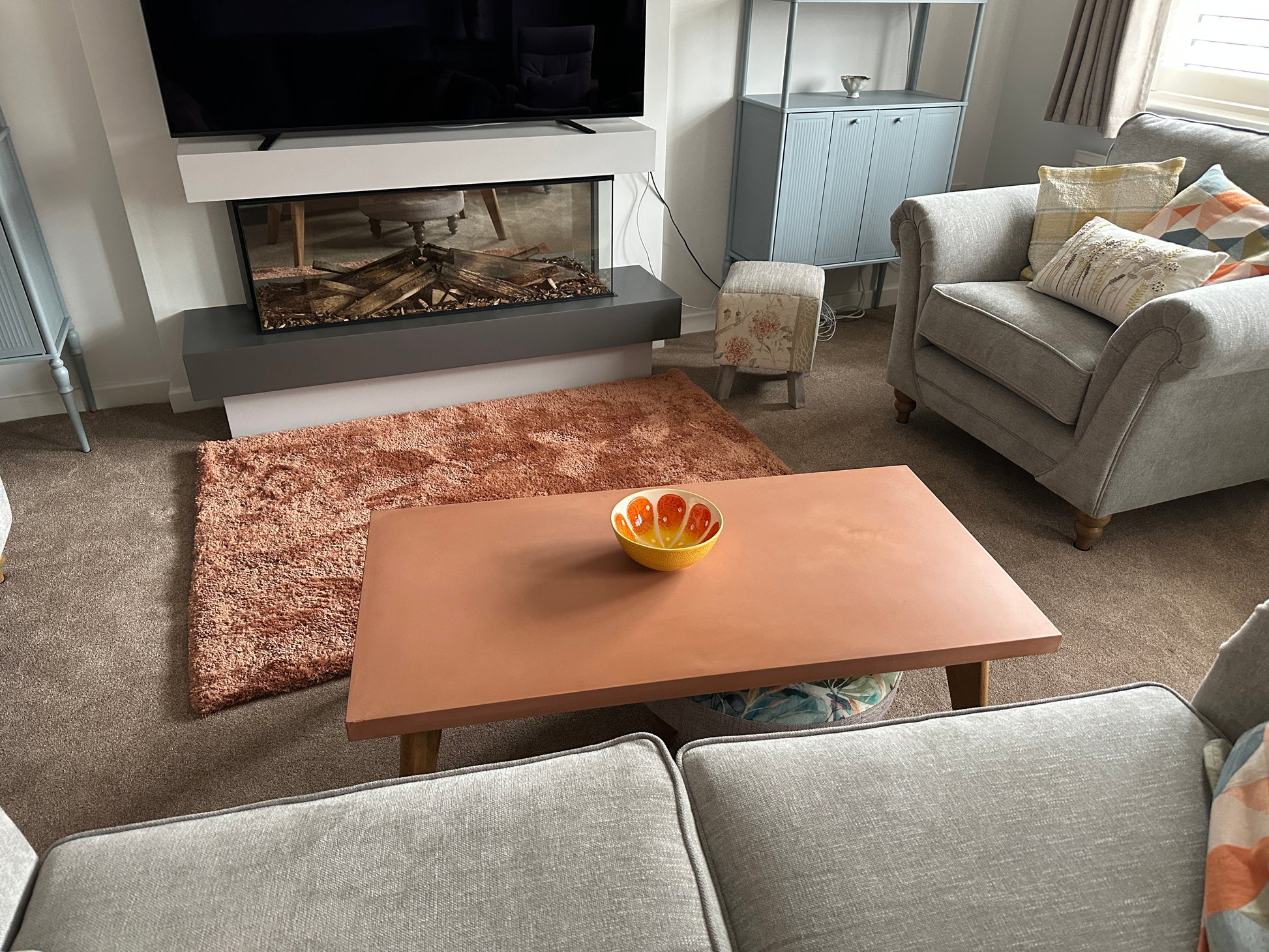 Living room with a fireplace, TV, and a bowl of fruit on a concrete coffee table.