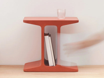 Red side table with books and a glass on a light wooden floor.